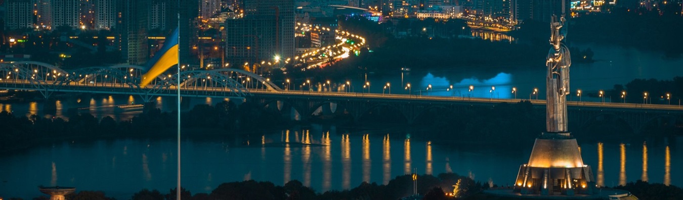 Kyiv skyline at night with the Ukrainian flag and the Motherland Monument overlooking the Dnipro River, symbolizing Hogan Lovells’ landmark High Court victory for PrivatBank in its $2 billion fraud case.